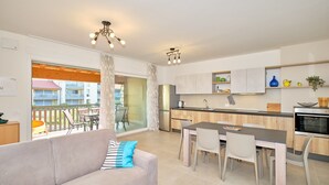 A modern apartment with a living room, dining area, kitchen, and a balcony with a view of buildings.