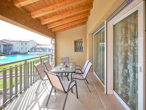 Een balkon met een tafel en stoelen, een zwembad en uitzicht op gebouwen.