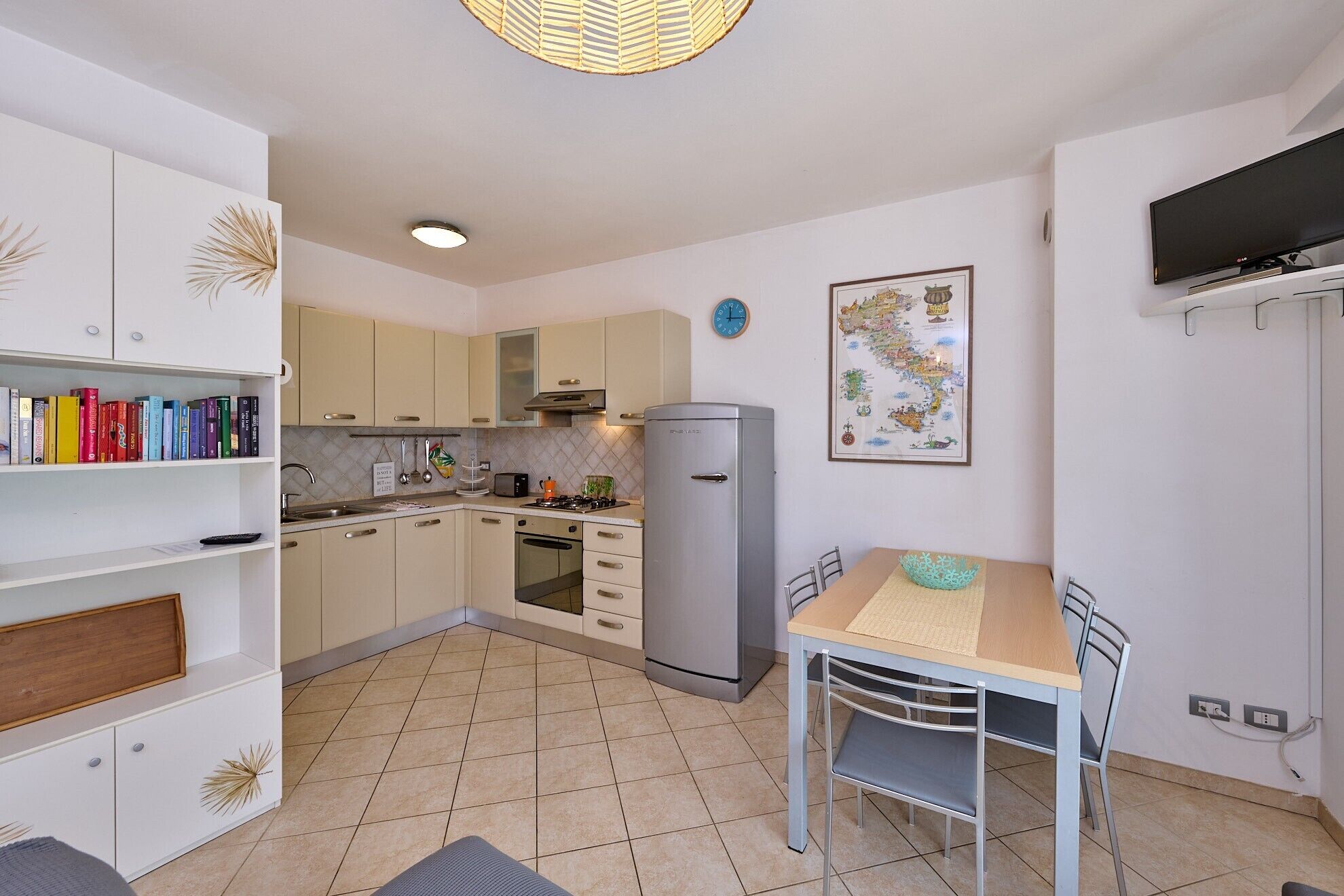 A compact kitchen with a dining area, a refrigerator, and a wall-mounted TV.
