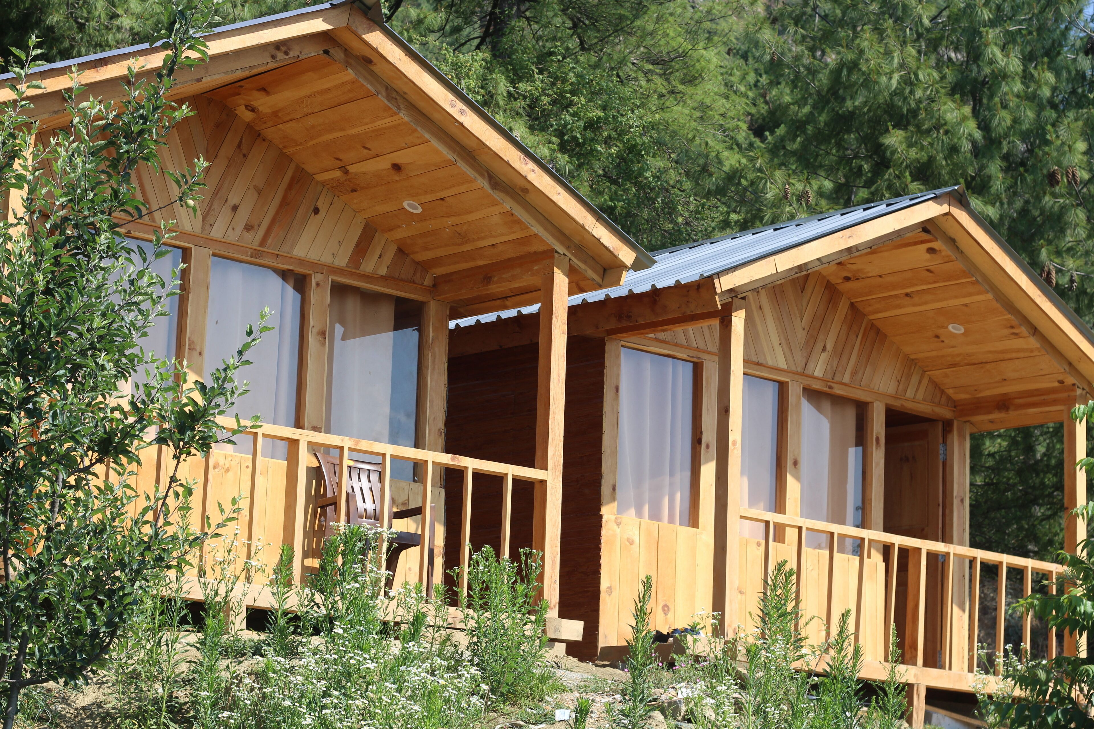 A wooden cabin with a balcony, large windows, and a view of the surrounding forest.