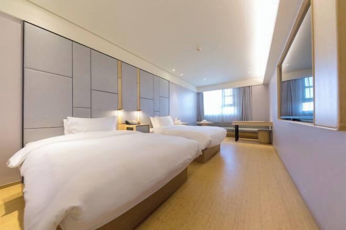 A modern hotel room with a large bed, bedside tables, a desk, and a large window.