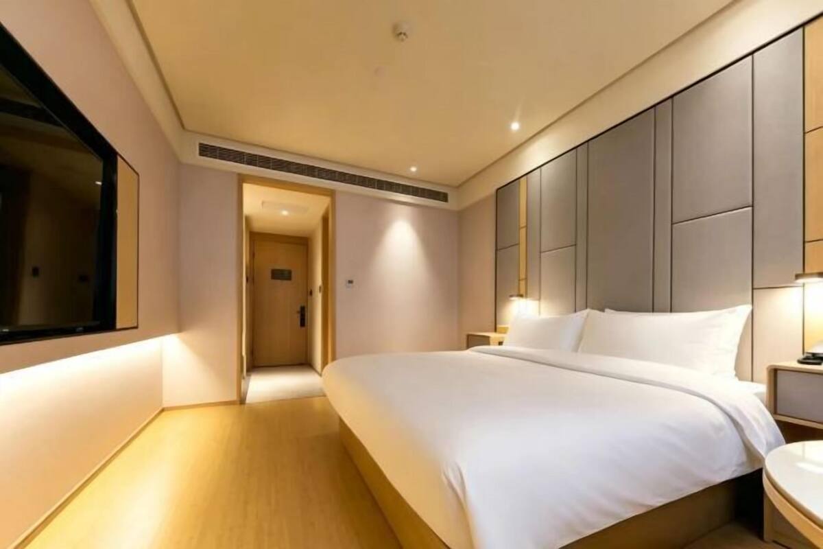 A modern hotel room with a large bed, a bedside table, a nightstand, and a large mirror.