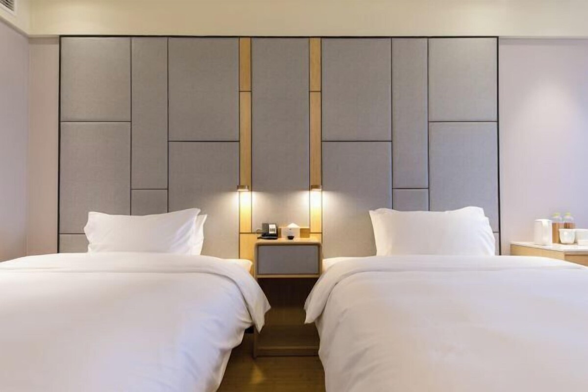 Una habitación de hotel con dos camas, una mesita de noche con lámpara y un diseño de panel en la pared.