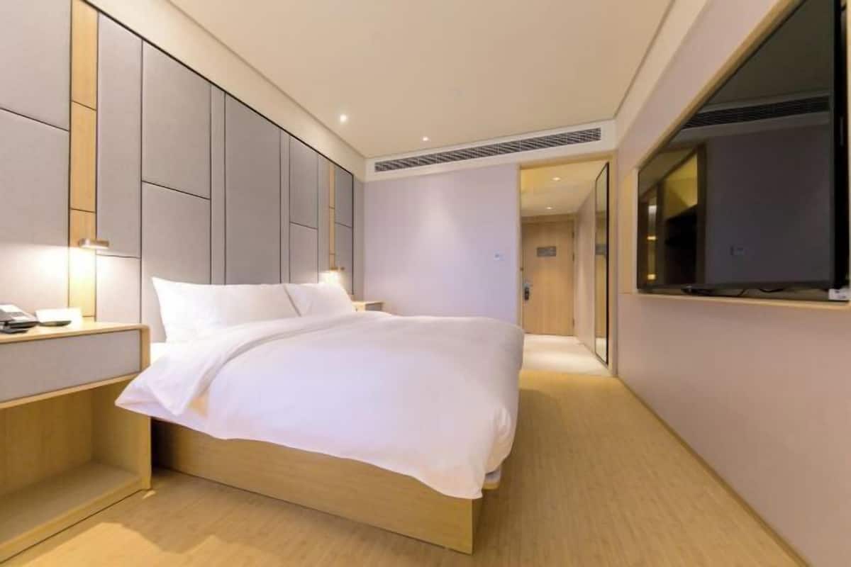 Quarto de hotel moderno com uma cama grande, uma mesinha de cabeceira com luminária e um espelho grande na parede.