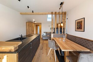 A modern kitchen with wooden accents, a dining area with a bench, and a view of the living room.