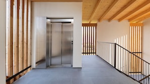 Un couloir avec un ascenseur métallique, des lambris en bois sur les murs et un sol carrelé.
