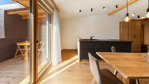 Une cuisine moderne avec des poutres en bois, un coin repas avec une table et des chaises, et une grande fenêtre.