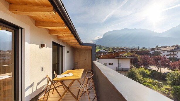 A balcony with a wooden table and chairs, overlooking a residential area with houses and mountains. - Apartment 'Panorama Loft Meran' with Mountain View, Private Terrace and Wi-Fi (Fié allo Sciliar)
