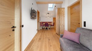 A modern interior with wooden flooring, a grey sofa, a dining area with a table and chairs, and a TV mounted on the wall. - Apartment 'Panorama Loft Meran' with Mountain View, Private Terrace and Wi-Fi (Fié allo Sciliar)