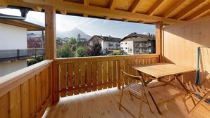 A wooden balcony with a table and chair, overlooking a mountain and buildings. - Studio Apartment 'Gardena' with Mountain View, Shared Garden and Wi-Fi (Fié allo Sciliar)