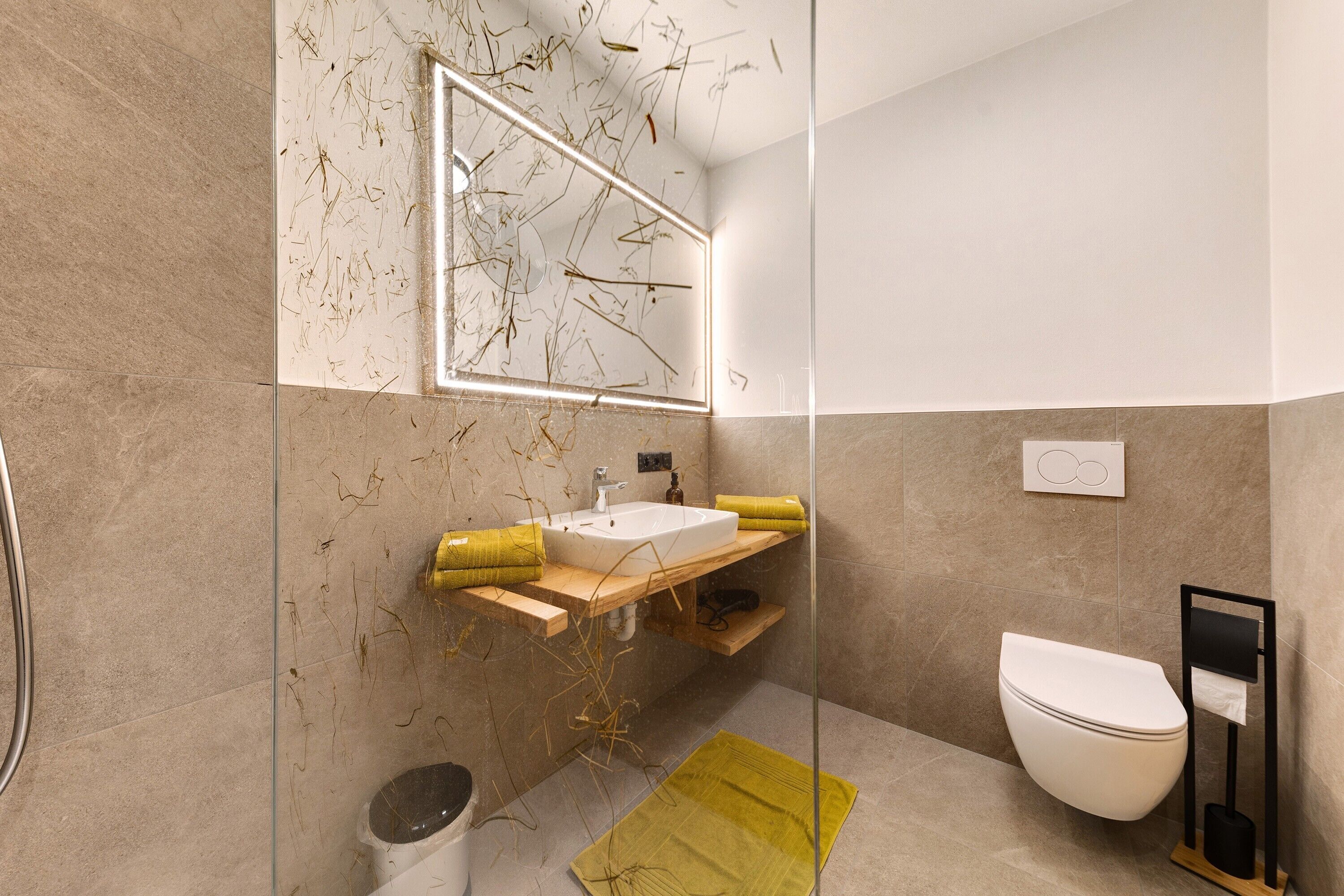 A modern bathroom with a glass shower enclosure, a white sink with a wooden countertop, a toilet, and a mirror with a unique design.