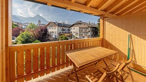 Un balcon en bois avec une table et des chaises, donnant sur une ville avec ses bâtiments et ses montagnes.