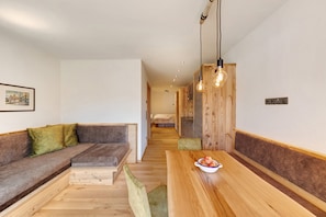 A modern interior with a wooden bench, a dining table with a bowl of fruit, and a hallway leading to a bedroom.