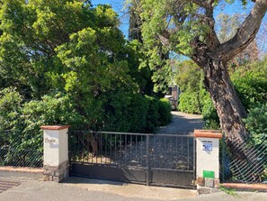 Une entrée fermée par un portail en métal, un mur en briques et un arbre.