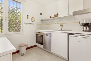 Una cucina moderna con mobili bianchi, lavastoviglie, forno e una finestra vista alberi.