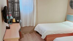 A hotel room with two beds, a desk, a chair, a small table with a lamp, and a window with curtains. - Yujiagui Hostel (Shanghai)