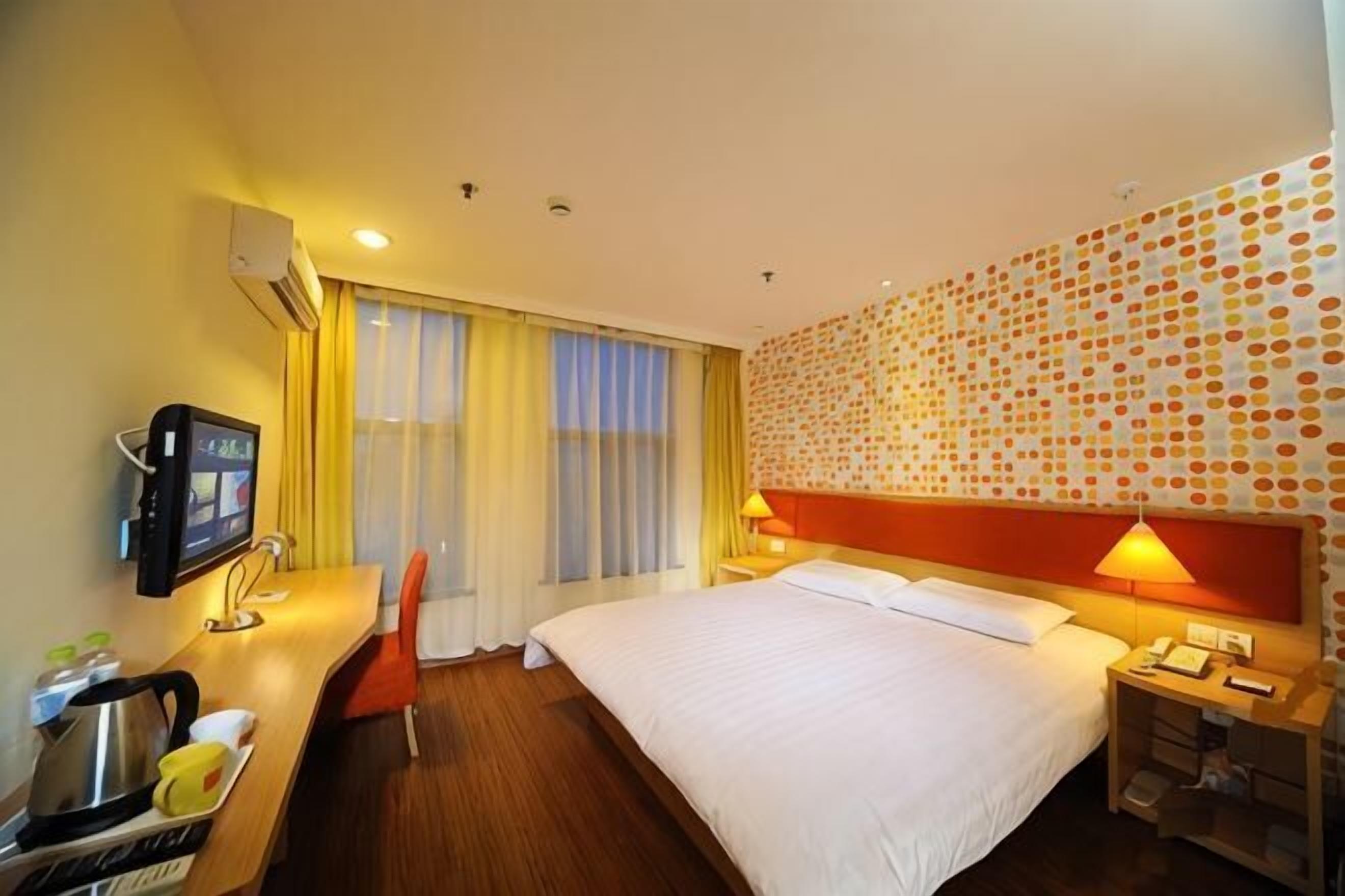 A hotel room with a bed, a desk with a chair, a TV, and a wall with a patterned design.
