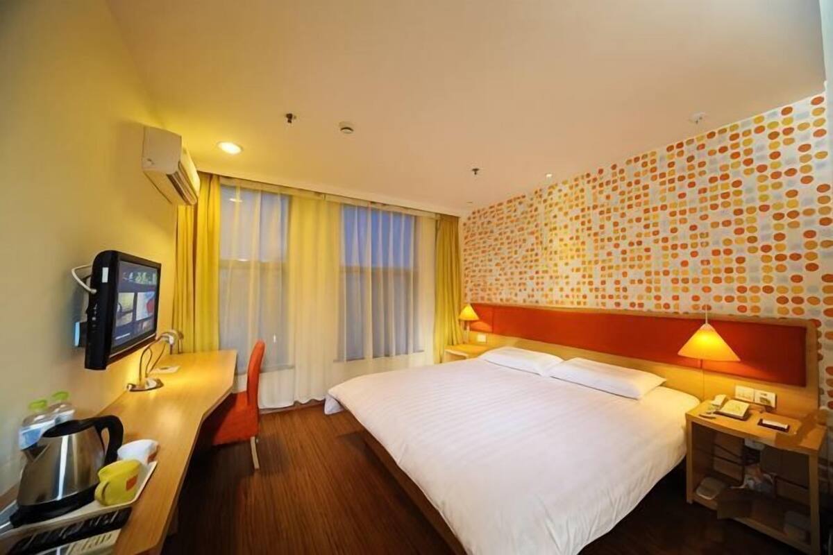 A hotel room with a bed, a desk with a chair, a TV, and a wall with a patterned design.