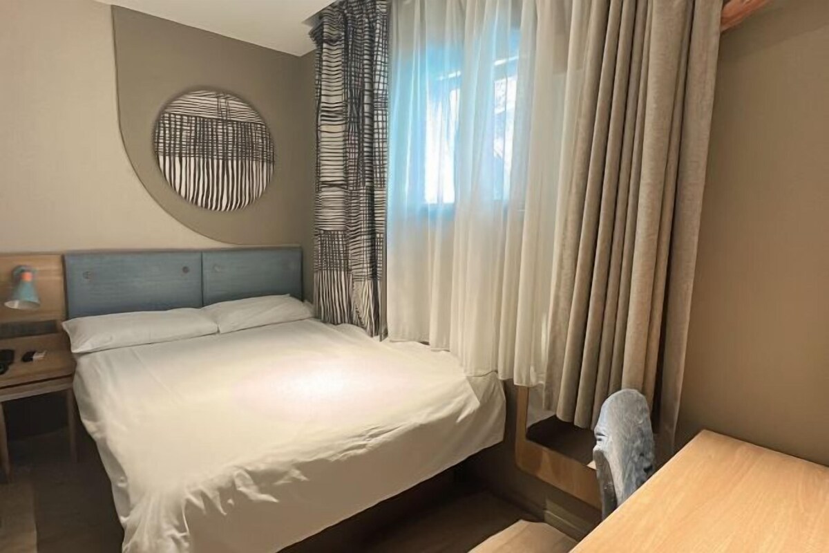 A bedroom with a bed, a nightstand, a round wall decoration, and a window with curtains.
