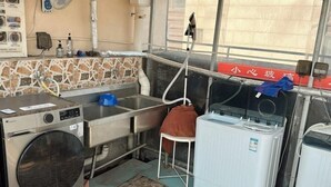 A laundry room with a washing machine, a dryer, a sink, and a fan. - Yujiagui Hostel (Shanghai)