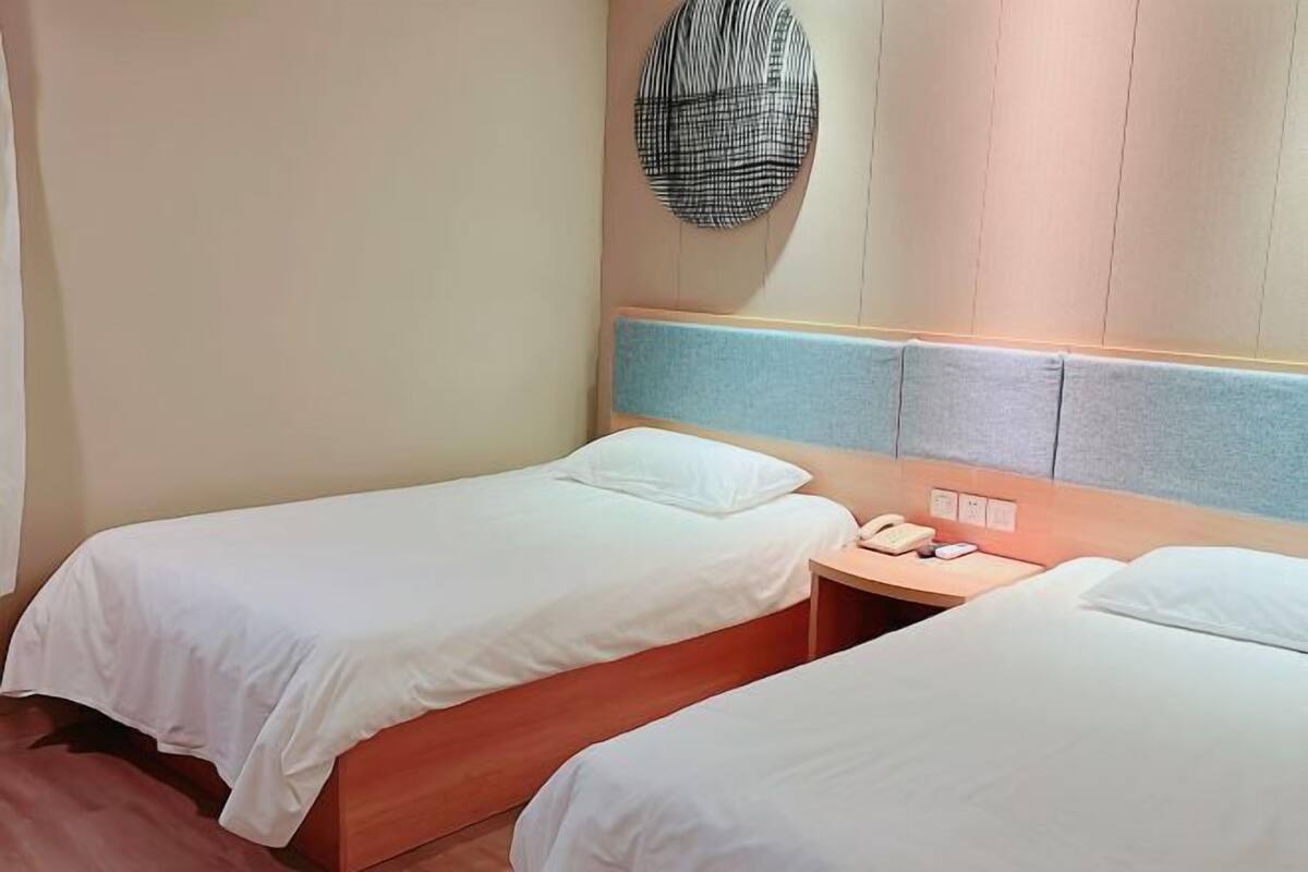 A hotel room with two single beds, a small bedside table with a phone, and a wall-mounted light fixture.