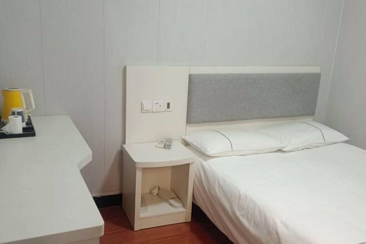 A hotel room with a bed, a bedside table, a lamp, and a power outlet.