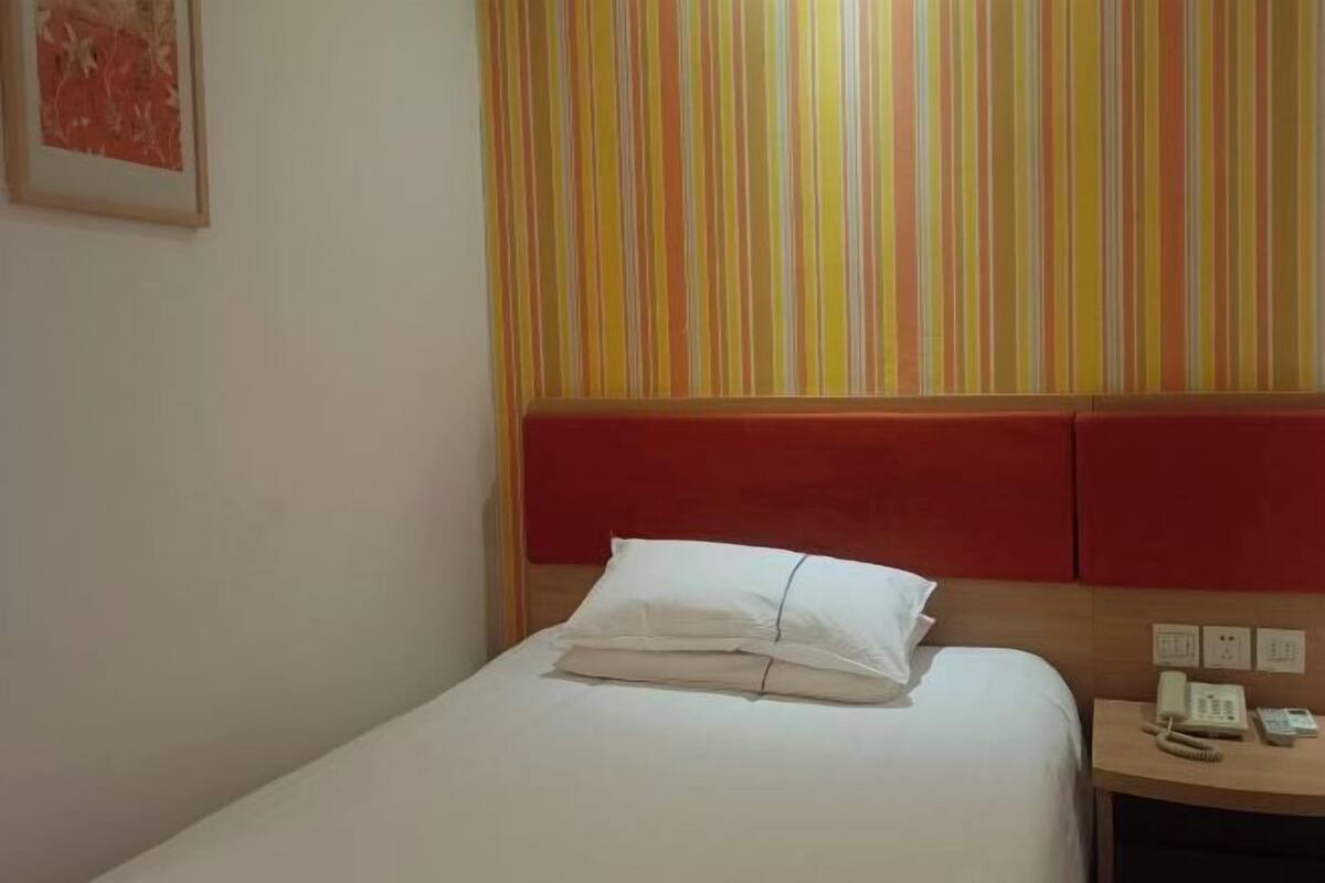 A hotel room with a bed, a bedside table with a phone, and a striped wall.