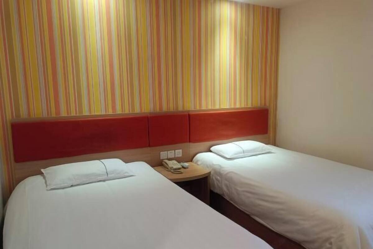 A hotel room with two single beds, a striped wall, a red headboard, and a bedside table with a phone.