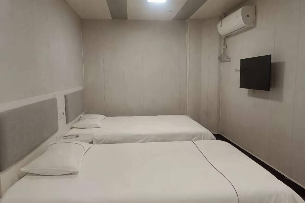 A room with two beds, a flat-screen TV, and an air conditioning unit.