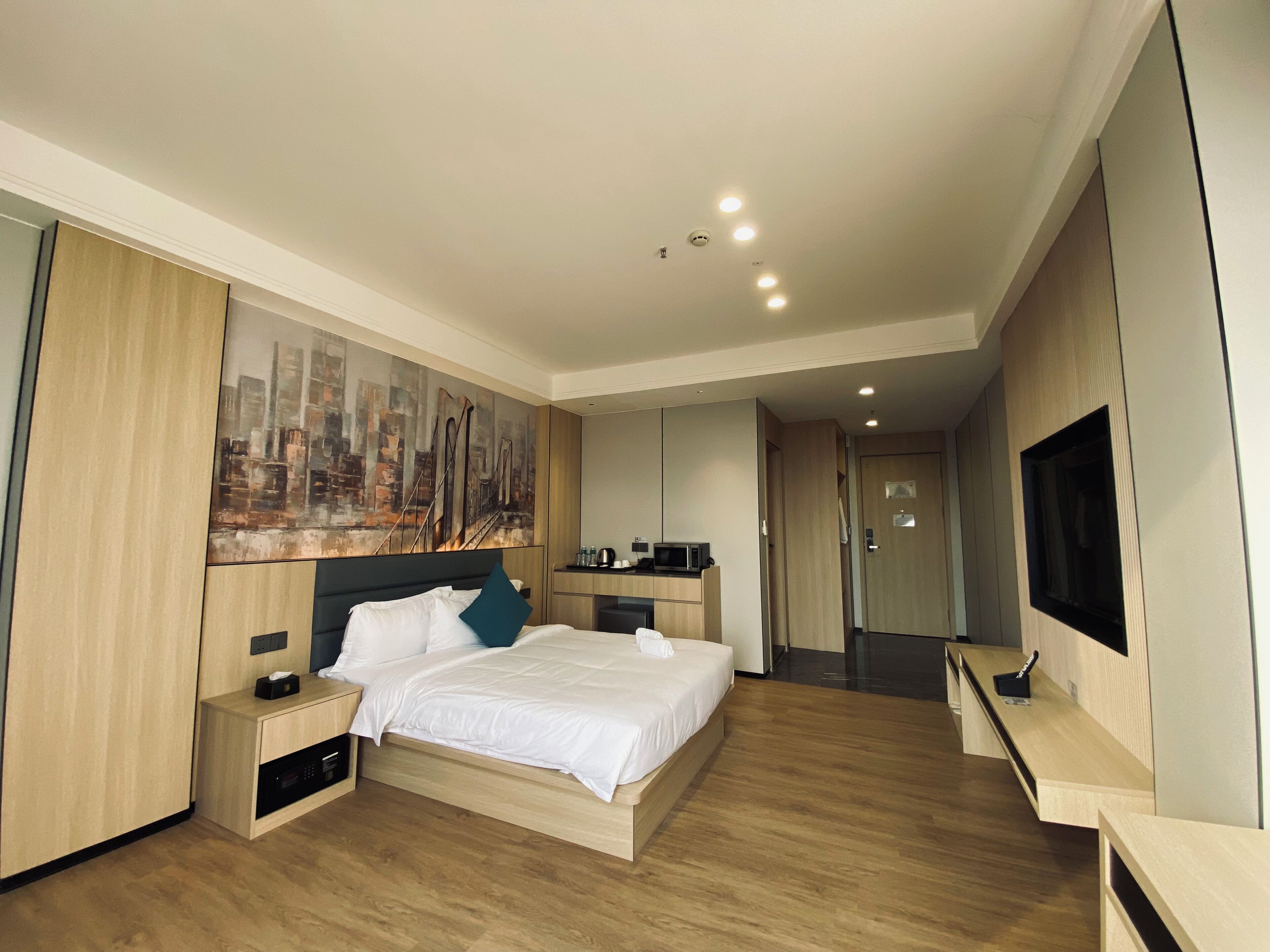 A modern hotel room with a bed, bedside tables, a painting, a desk, and a television.