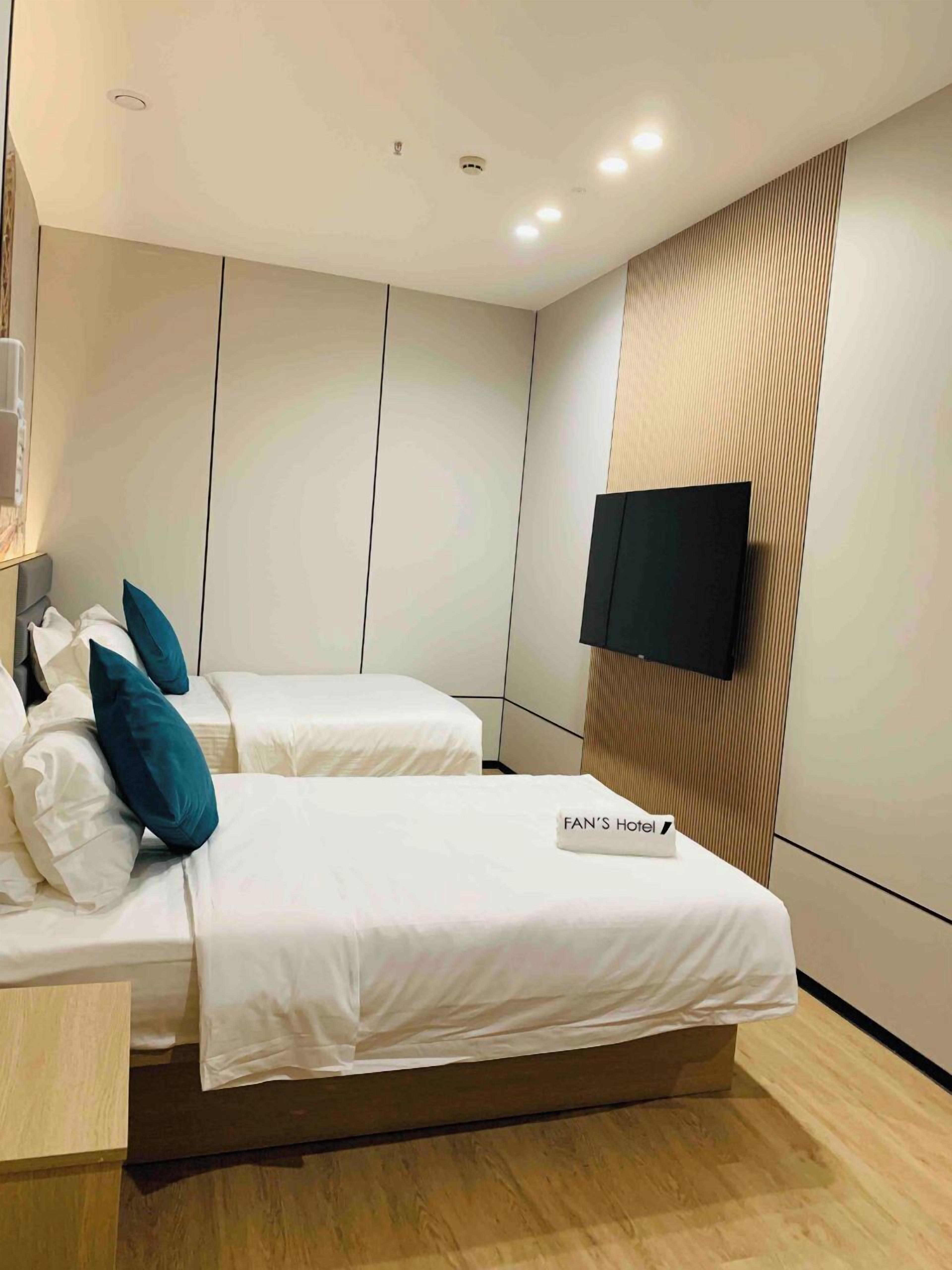 Habitación de hotel con dos camas, un televisor de pantalla plana montado en la pared y suelo de madera.