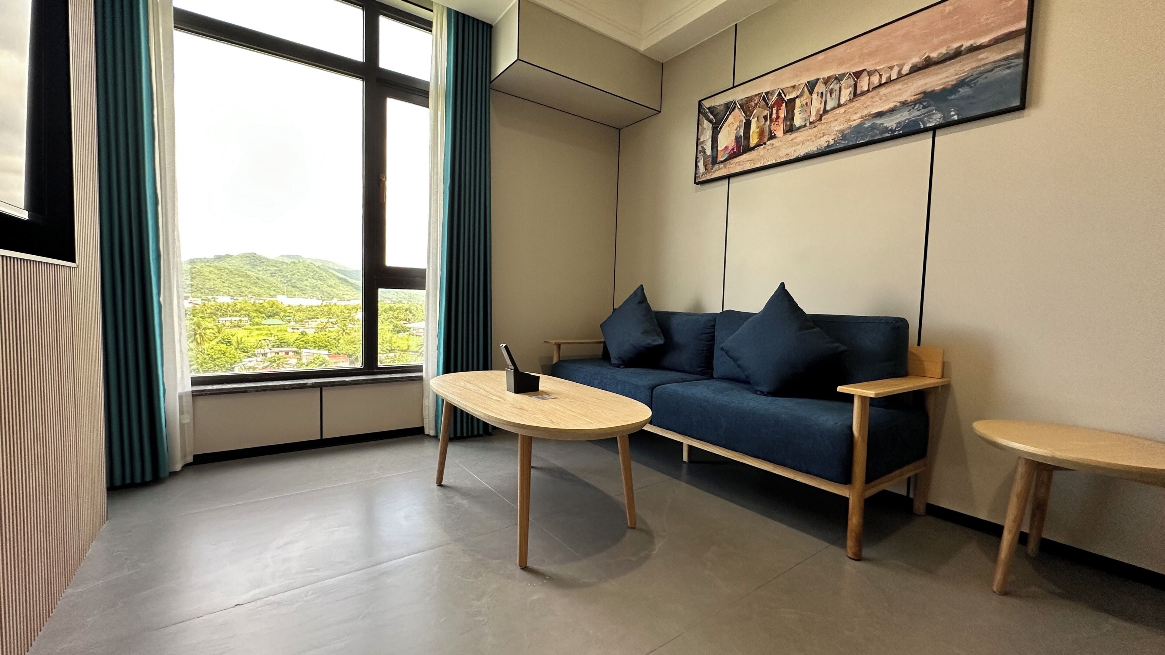 A modern living room with a sofa, a coffee table, and a small side table. A painting is on the wall, and there's a window with curtains.
