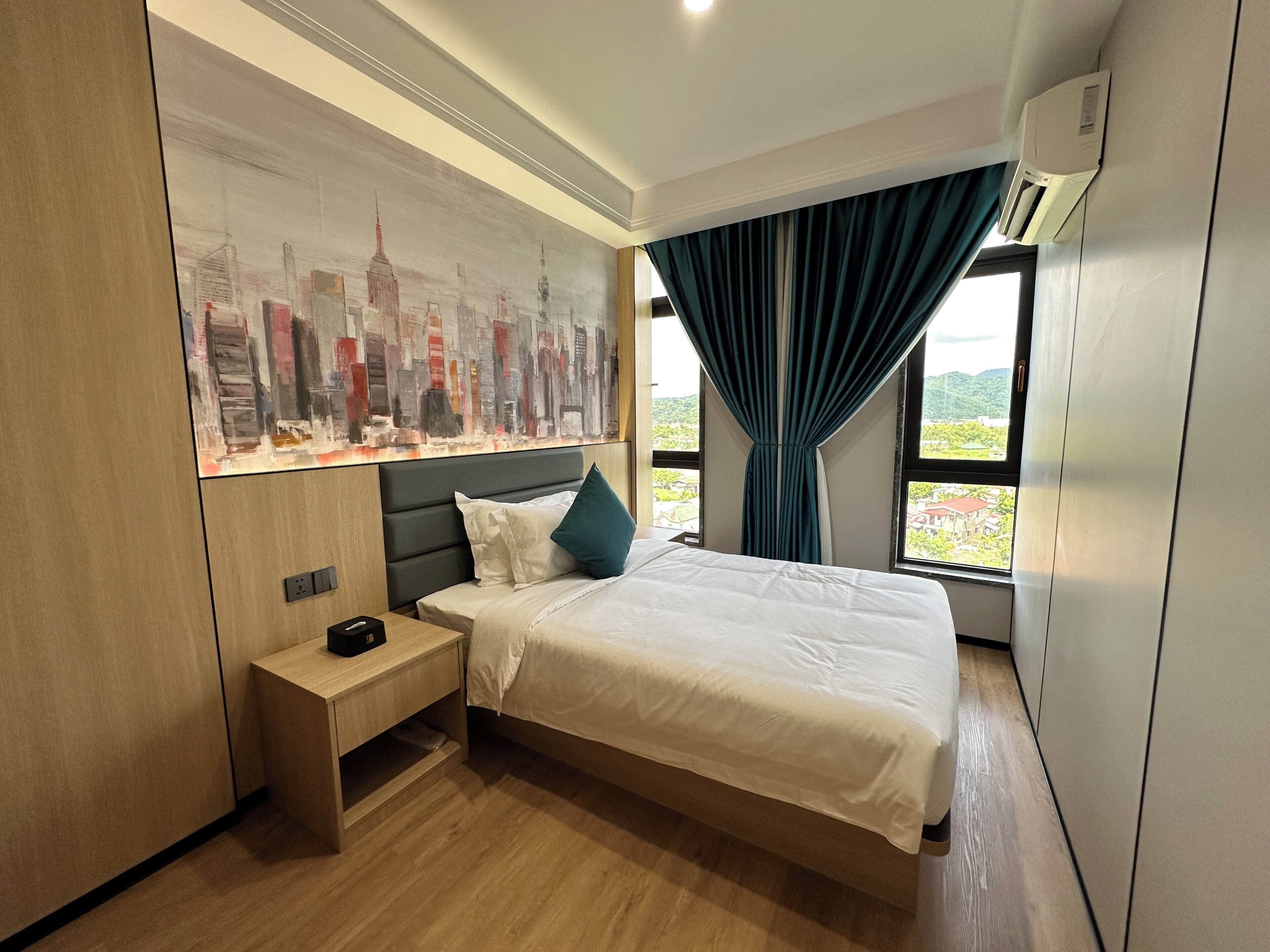 Una camera d'albergo con un letto, un comodino e un dipinto con vista sulla città.