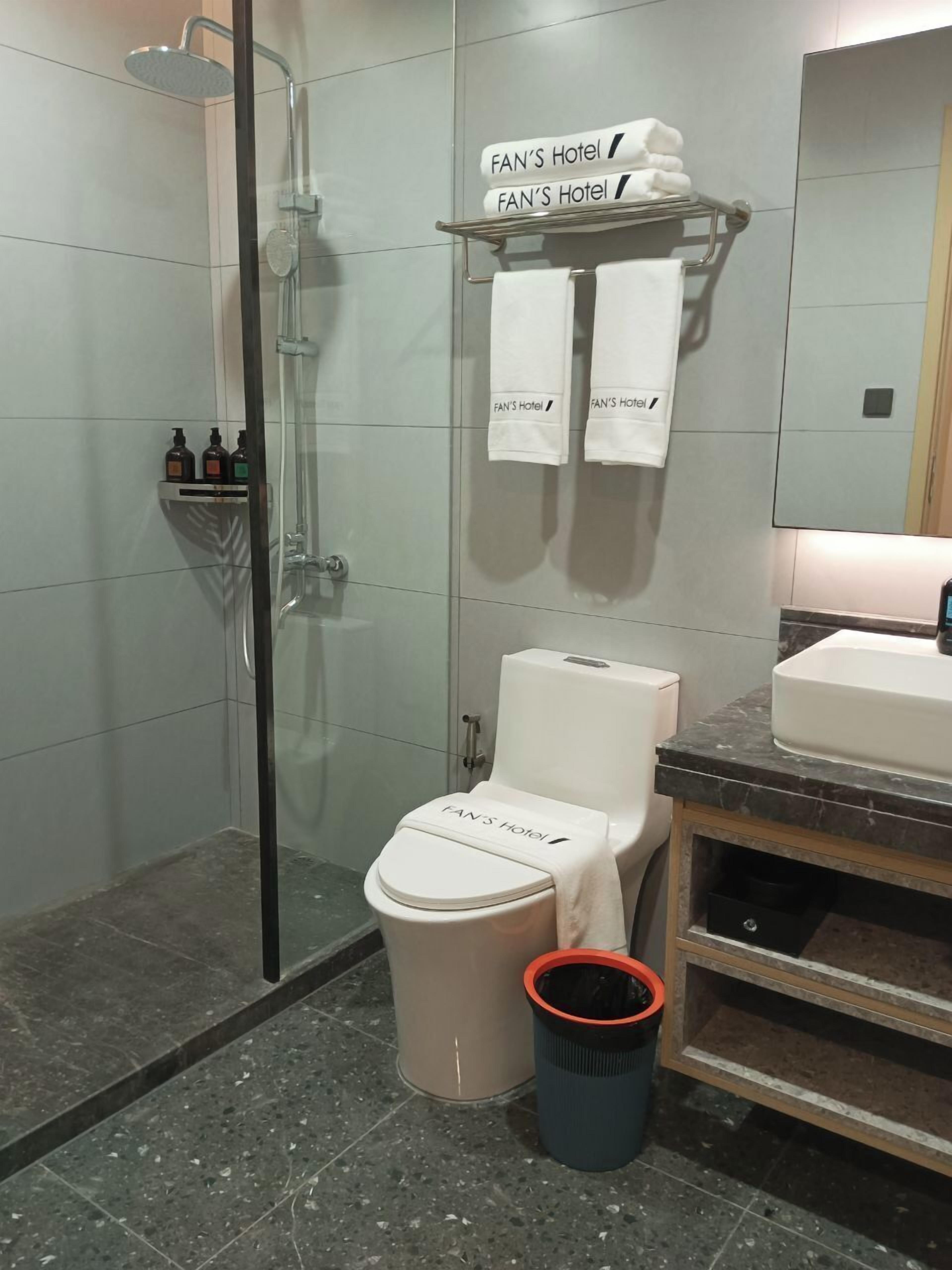 Un baño moderno con ducha envuelta en vidrio, un inodoro con una toalla y un lavamanos con encimera de mármol.