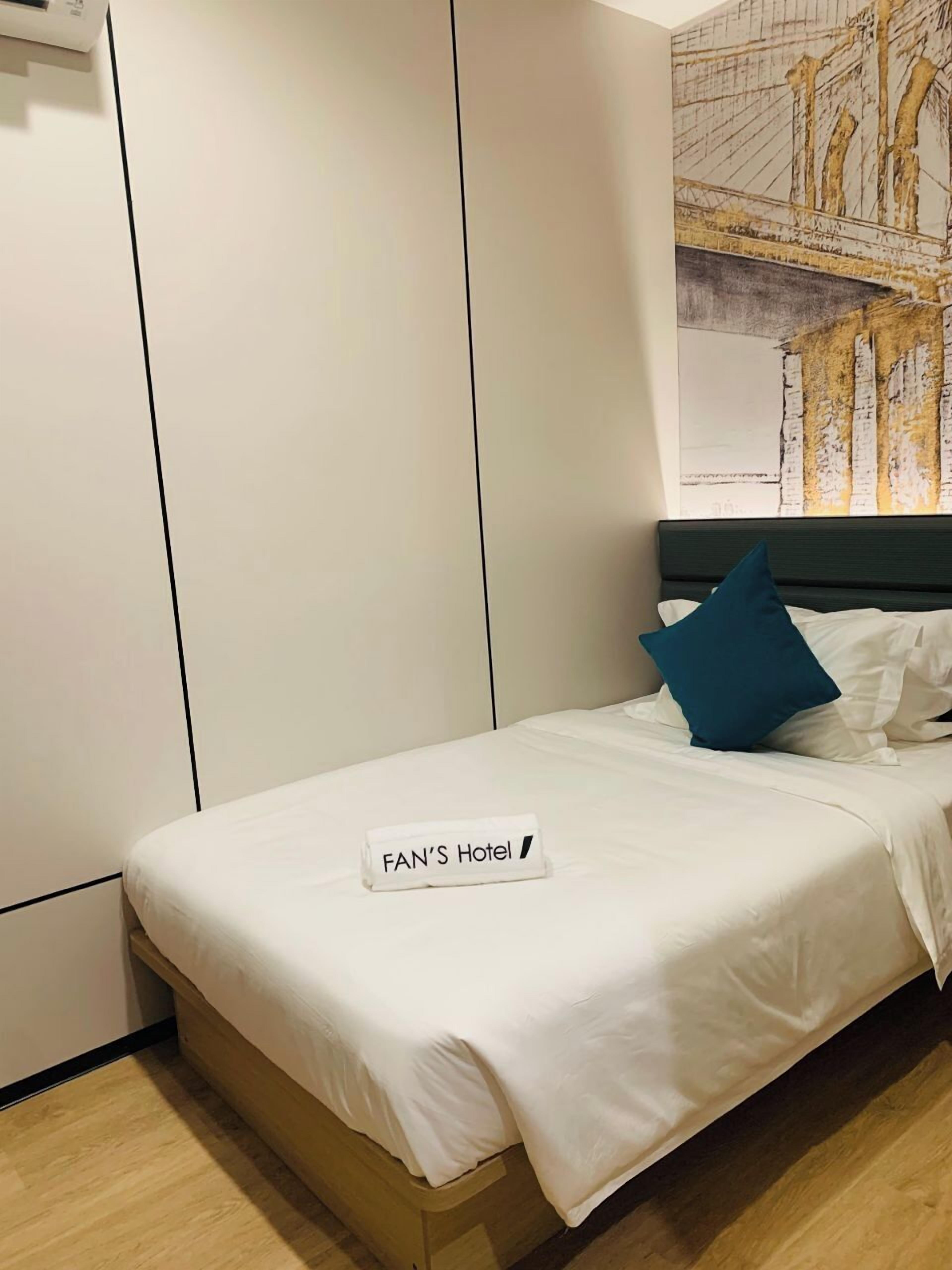 Ein Hotelzimmer mit Bett, Kopfstück, Wand mit Gemälde und einem Schild auf dem Bett.