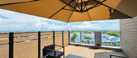 A balcony with a wooden floor, a black metal railing, and a large beige umbrella providing shade.