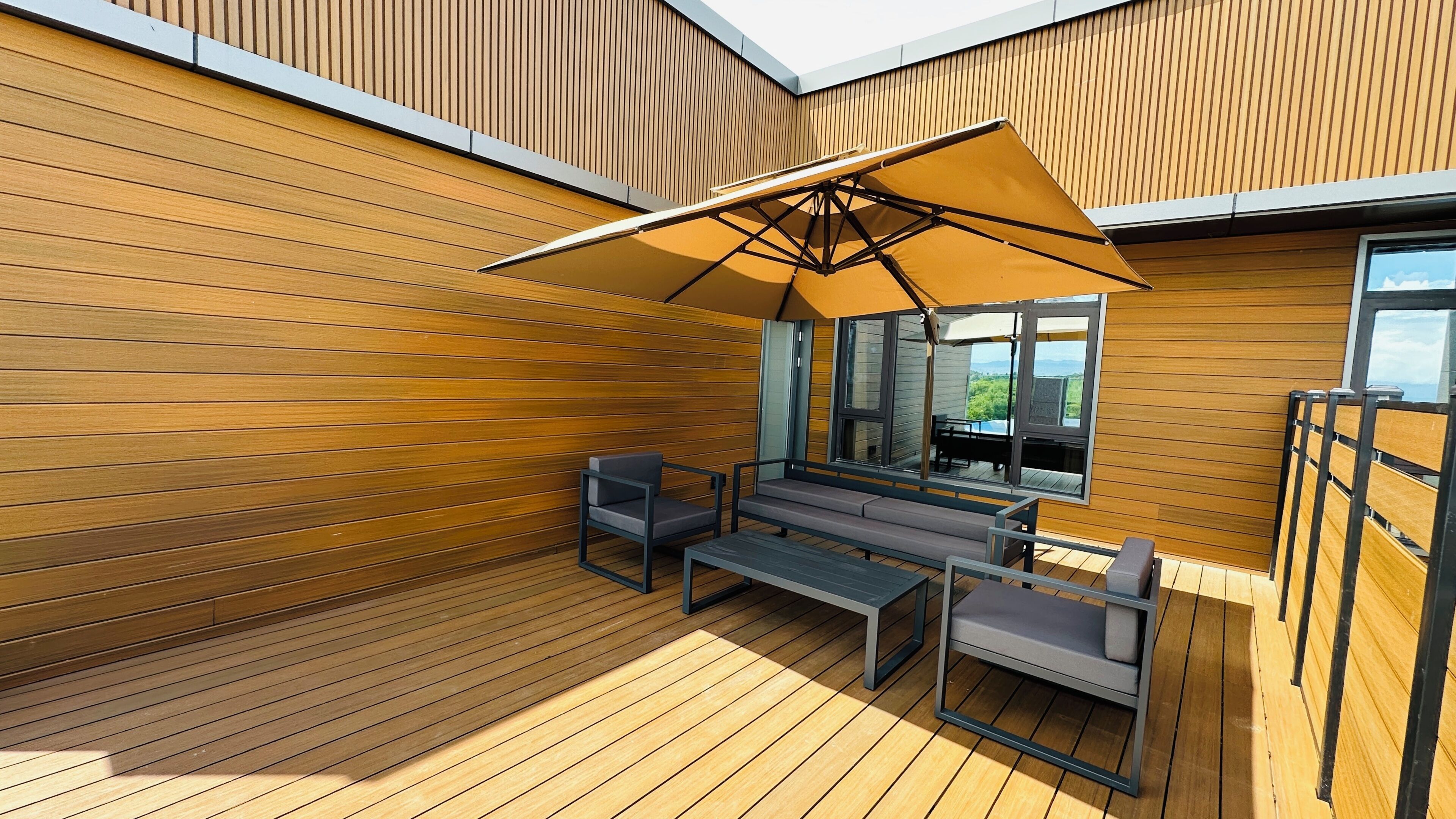 An outdoor deck with wooden flooring, a seating area with a table and chairs, and a large umbrella providing shade.