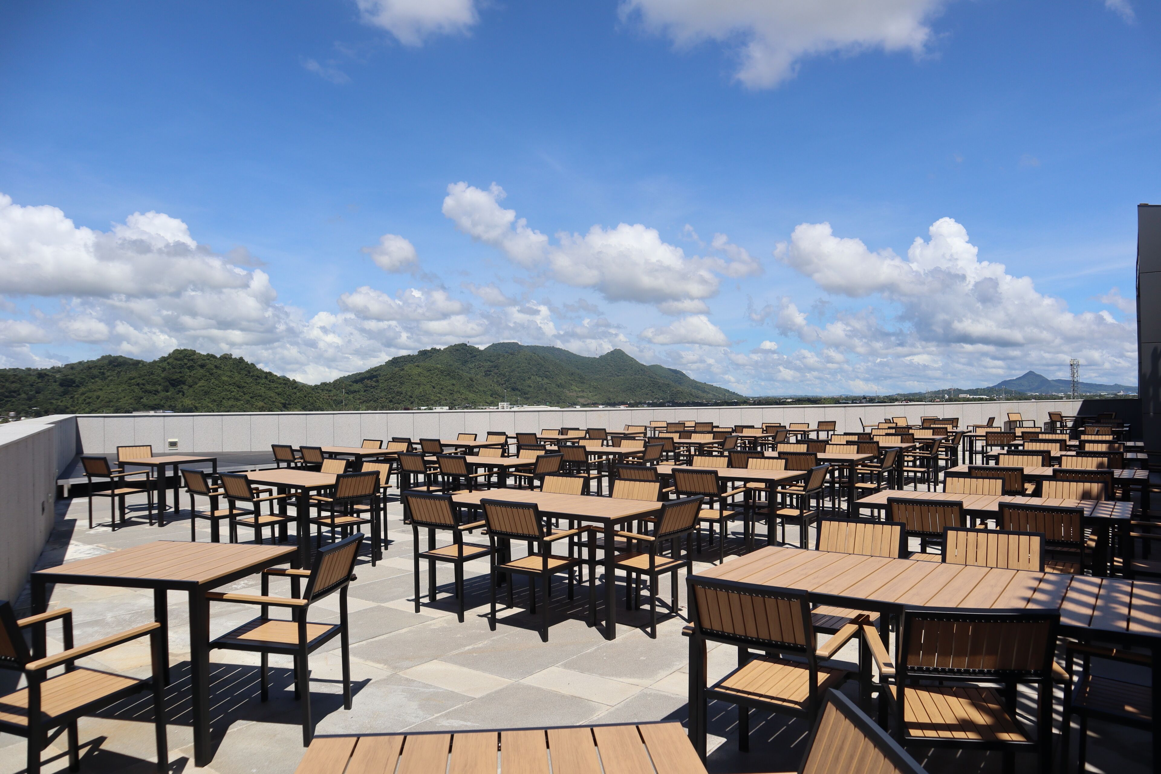 Terraza en la azotea con varias mesas y sillas, que ofrece vistas a montañas distantes.