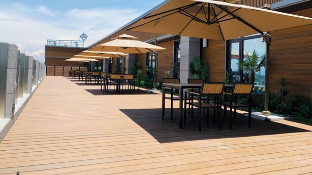 An outdoor patio with wooden flooring, beige umbrellas, and seating arrangements. - Fan's Hotel Palo (Palo)