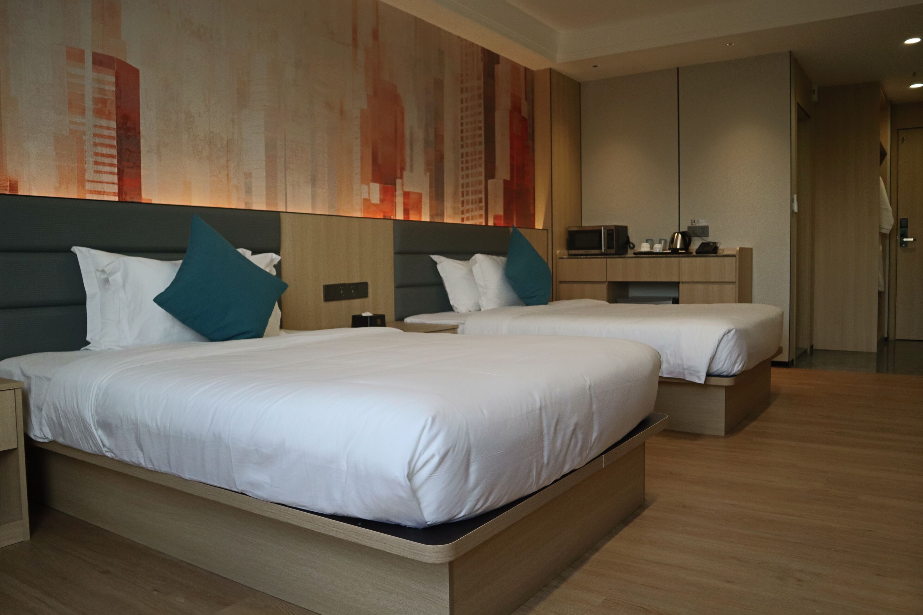 A hotel room with two beds, a bedside table, a nightstand, a desk, and a large abstract painting on the wall.