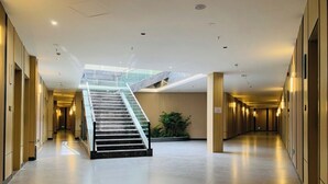 A spacious hotel corridor with a central staircase, modern lighting, and a plant in the middle. - Fan's Hotel Palo (Palo)