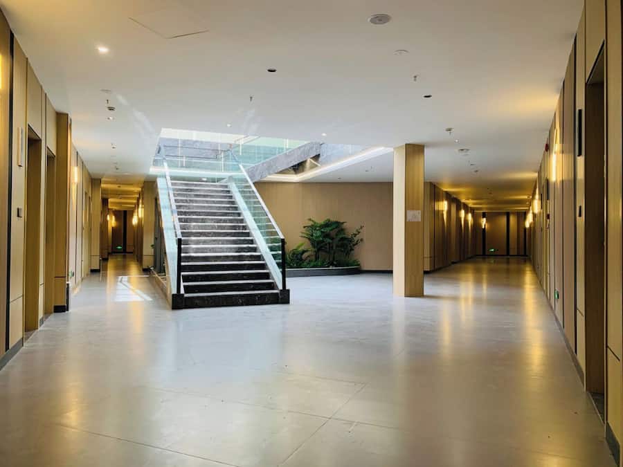 A spacious hotel corridor with a central staircase, modern lighting, and a plant in the middle.