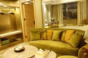 Habitación de hotel con sofá verde, una mesa redonda de centro, mesita de noche y una ventana con cortinas.