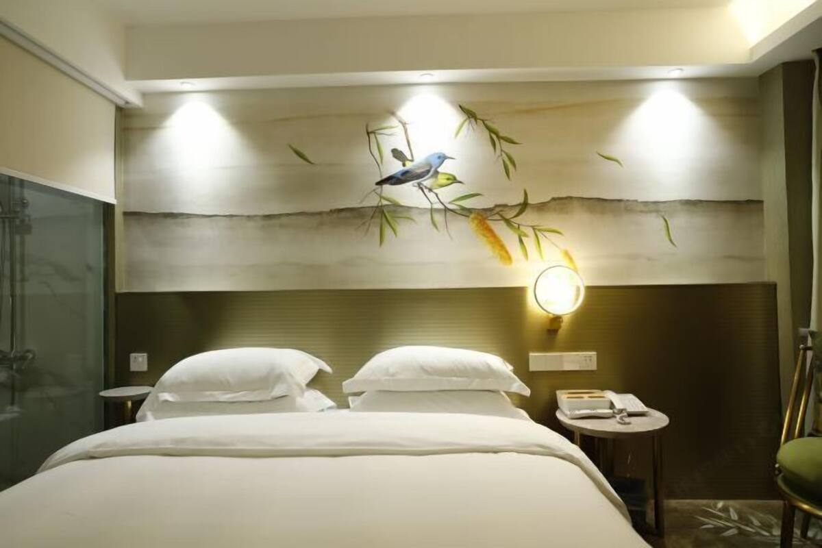 A hotel room with a bed, a bedside table with a lamp, a mirror, and a wall-mounted artwork of birds on branches.