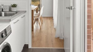Une cuisine moderne équipée d’un lave-linge, un coin repas avec une table et des chaises, et une vue sur un jardin grâce à une porte vitrée.