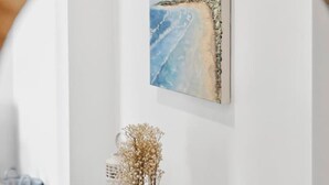Une pièce avec un mur blanc, un tableau représentant une plage, une console en bois sur laquelle est posé un vase de fleurs séchées, et un miroir qui reflète la scène.