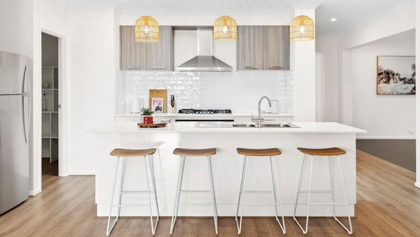 Une cuisine moderne dotée d’un îlot central, de tabourets de bar, de luminaires suspendus et d’une hotte de cuisine en acier inoxydable.