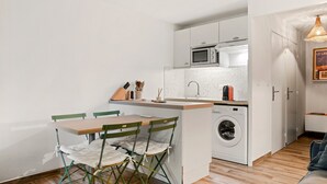 Una cocina compacta equipada con lavadora, microondas y lavamanos. Cuenta con una zona de comedor con mesa y sillas.