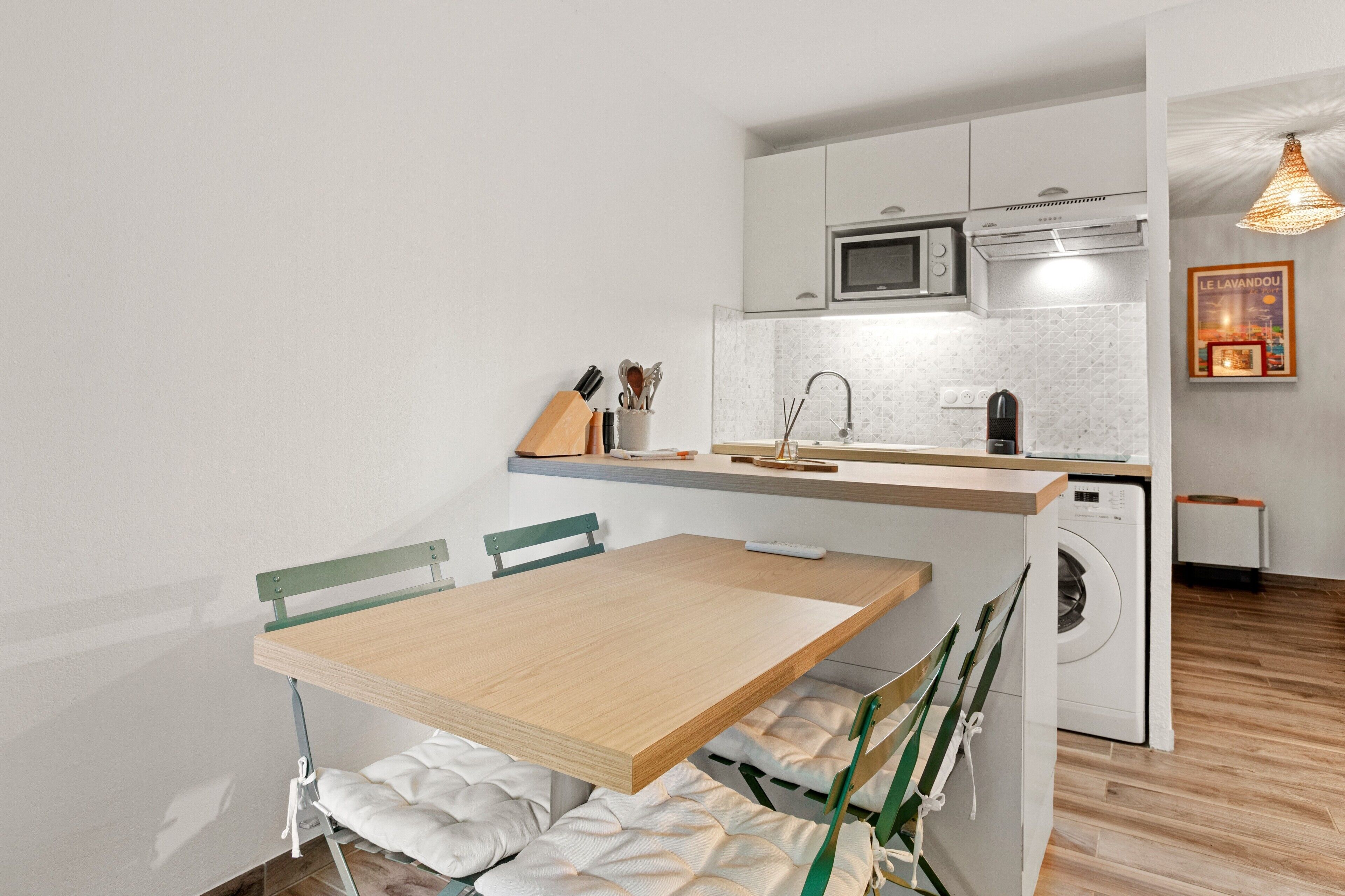 Een kleine keuken met een eethoek, een wasmachine en een hanglamp.