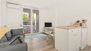 Un espacio habitable compacto con sofá, zona de comedor con mesa y sillas, cocina con mostrador y armarios, y puerta corrediza de vidrio que da a un área exterior.